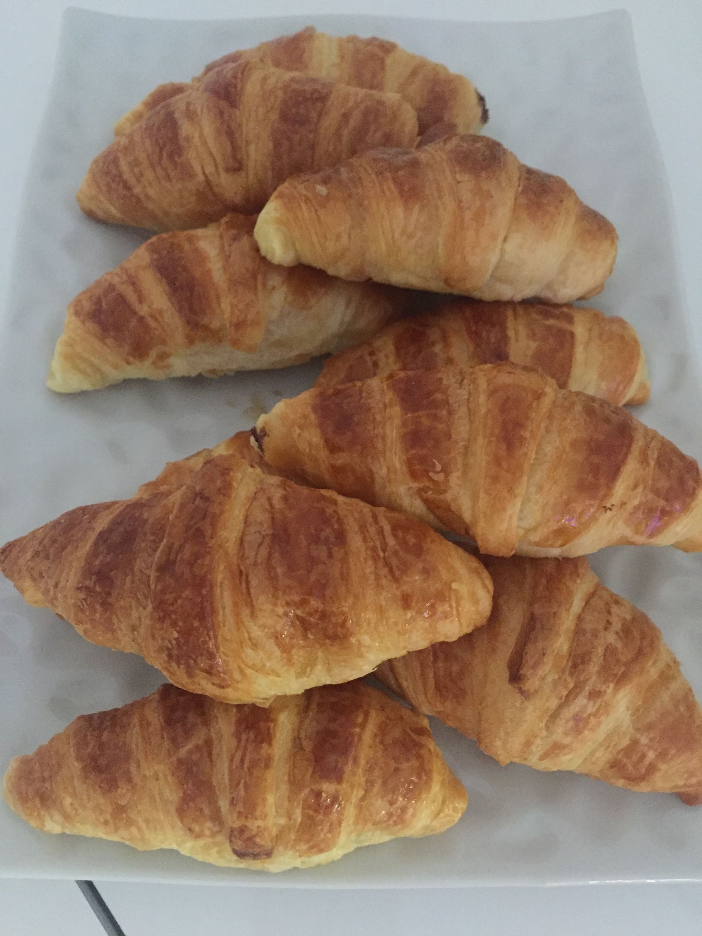 A tray of golden-brown croissants arranged on a white plate.