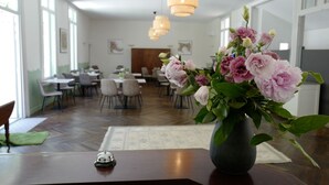 Un espace repas avec des tables et des chaises, un vase de fleurs posé sur une table et des luminaires suspendus au plafond.