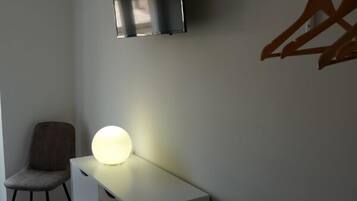 A modern room with a white desk, a chair, a hanging TV, and a wall-mounted clothes rack.