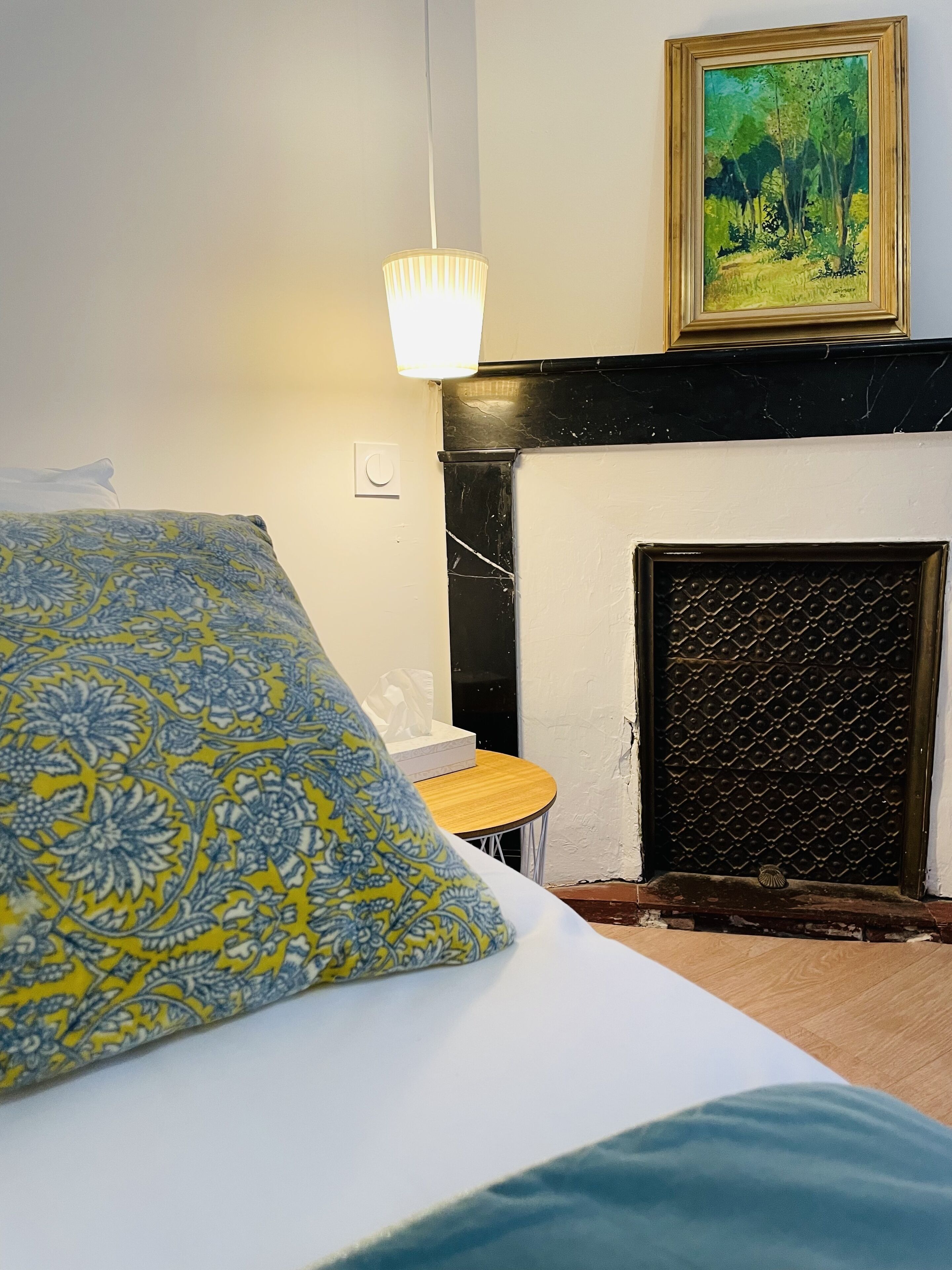 Une chambre à coucher avec un lit, une table de chevet, une lampe, un tableau et une cheminée.