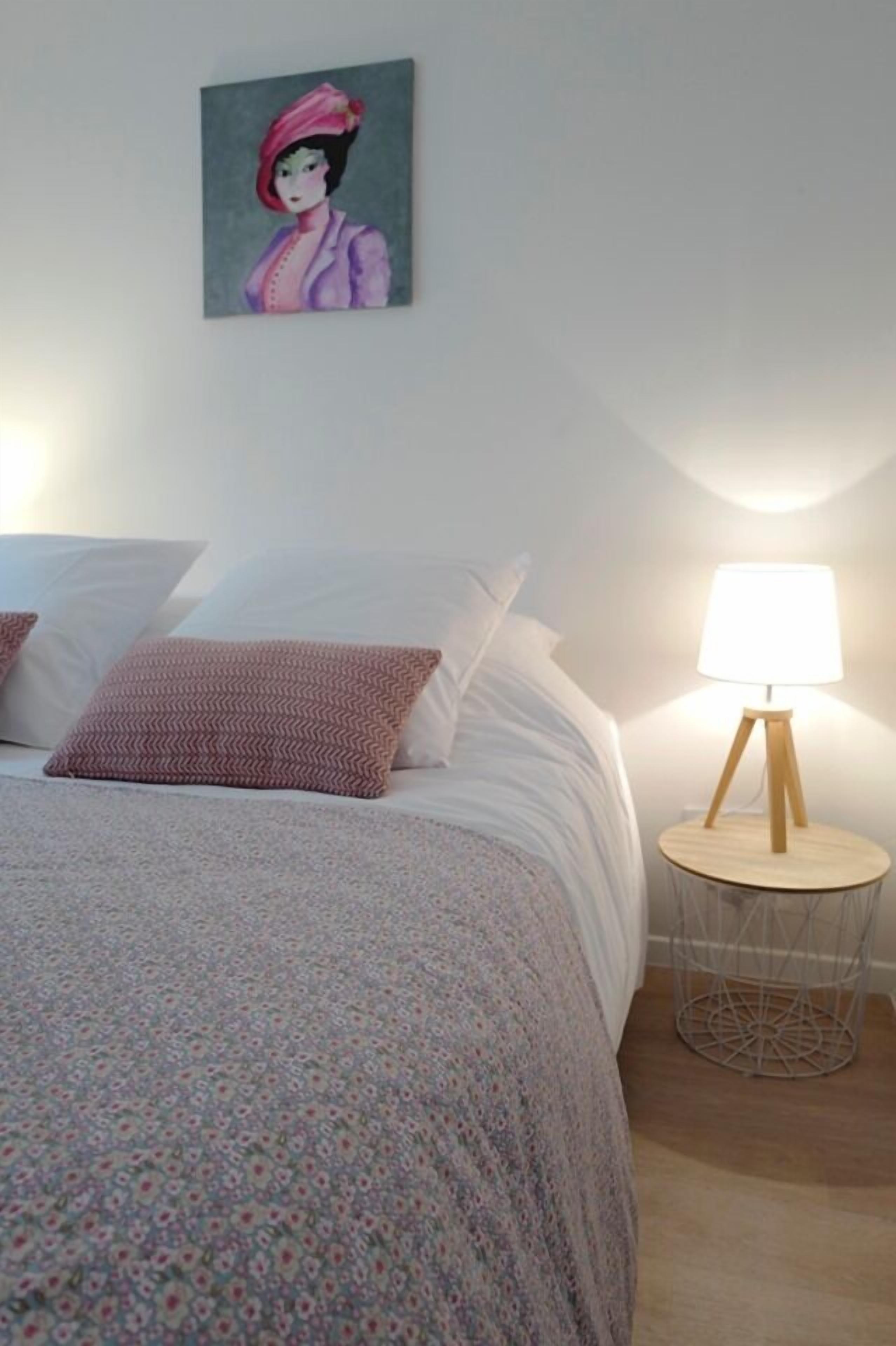 Una cama bien hecha con ropa de cama estampada, una mesita de noche pequeña con una lámpara y un cuadro colgado en la pared.