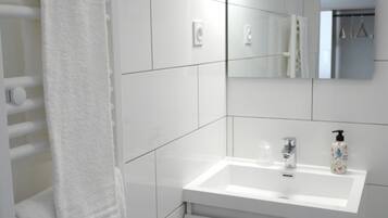 A modern bathroom with white tiles, a white sink, a mirror, and a towel rack.