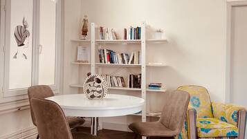 Una habitación con una mesa redonda blanca, dos sillas, una estantería y un sillón estampado.