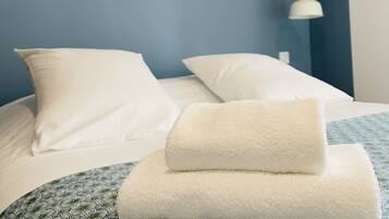 Camera d'albergo con un letto, cuscini bianchi, una parete blu, un quadro astratto bianco e una lampada bianca.
