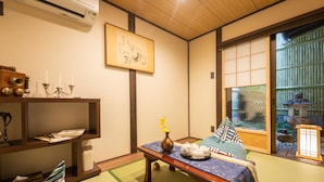 A traditional Japanese room with tatami flooring, a low table with a vase and teapots, a futon bed, and a sliding door leading to a garden. - KumoMachiya Goshohigashi (Kyoto)