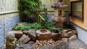 A traditional Japanese garden with bamboo walls, a stone lantern, and a rock arrangement. - KumoMachiya Goshohigashi (Kyoto)