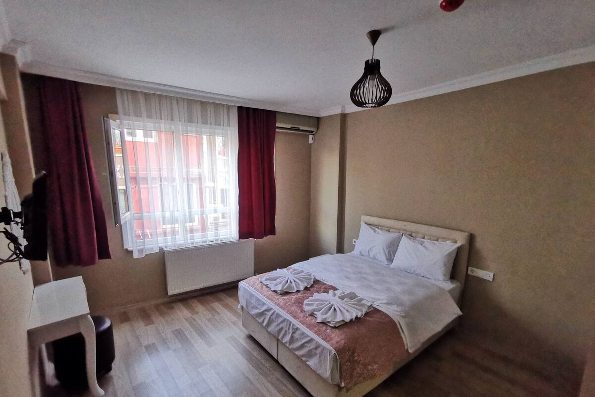 A bedroom with a bed, a radiator, a window with curtains, and a hanging light fixture.