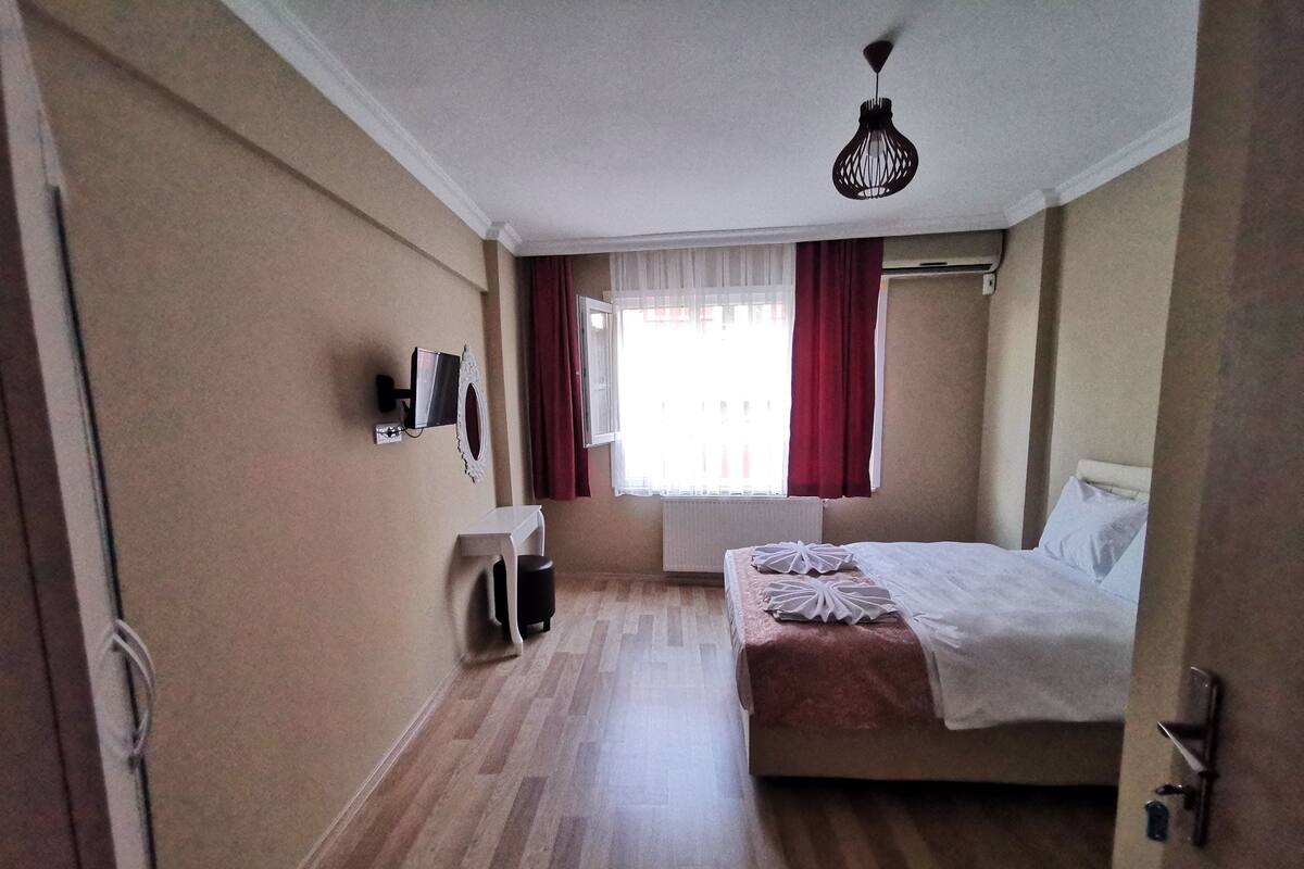 A hotel room with a bed, a small table, a TV, and a window with curtains.