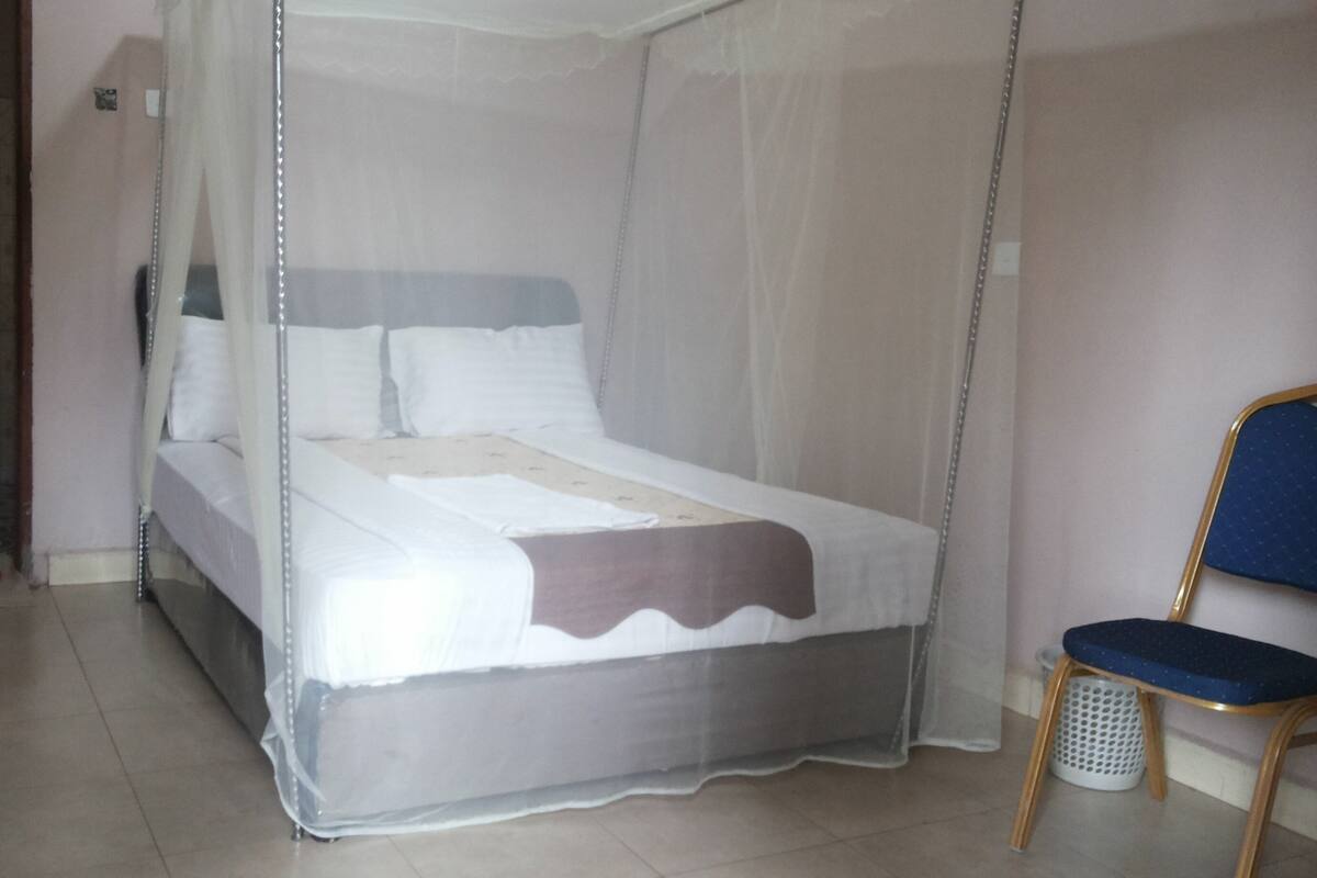 Una cama individual con dosel, una silla y una mesita con una cesta.