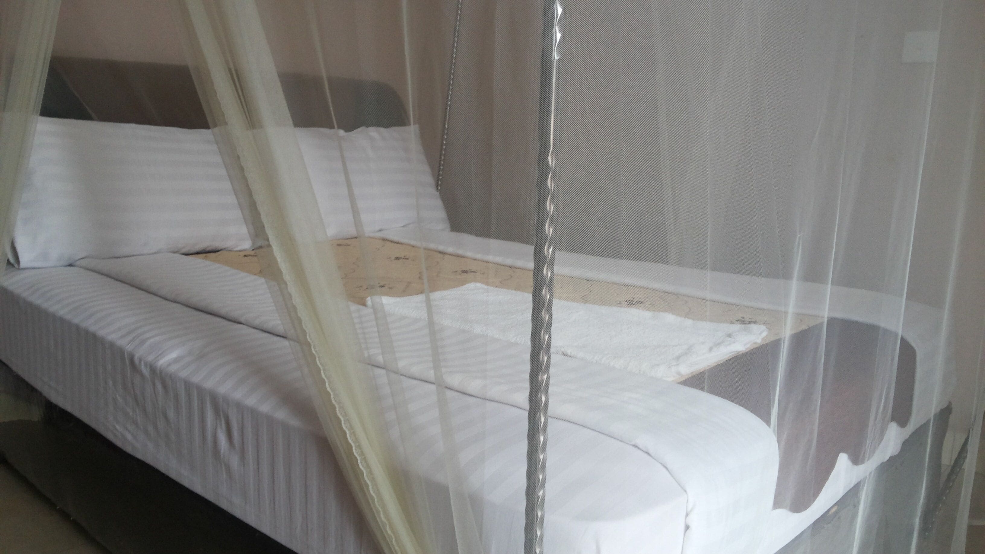 Una cama con ropa blanca y una mosquitera.