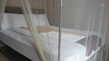 Una cama con ropa blanca y una mosquitera.