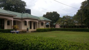 A building with a green roof, arched windows, and a well-maintained lawn. - Blue Dove Hotel (Koboko)