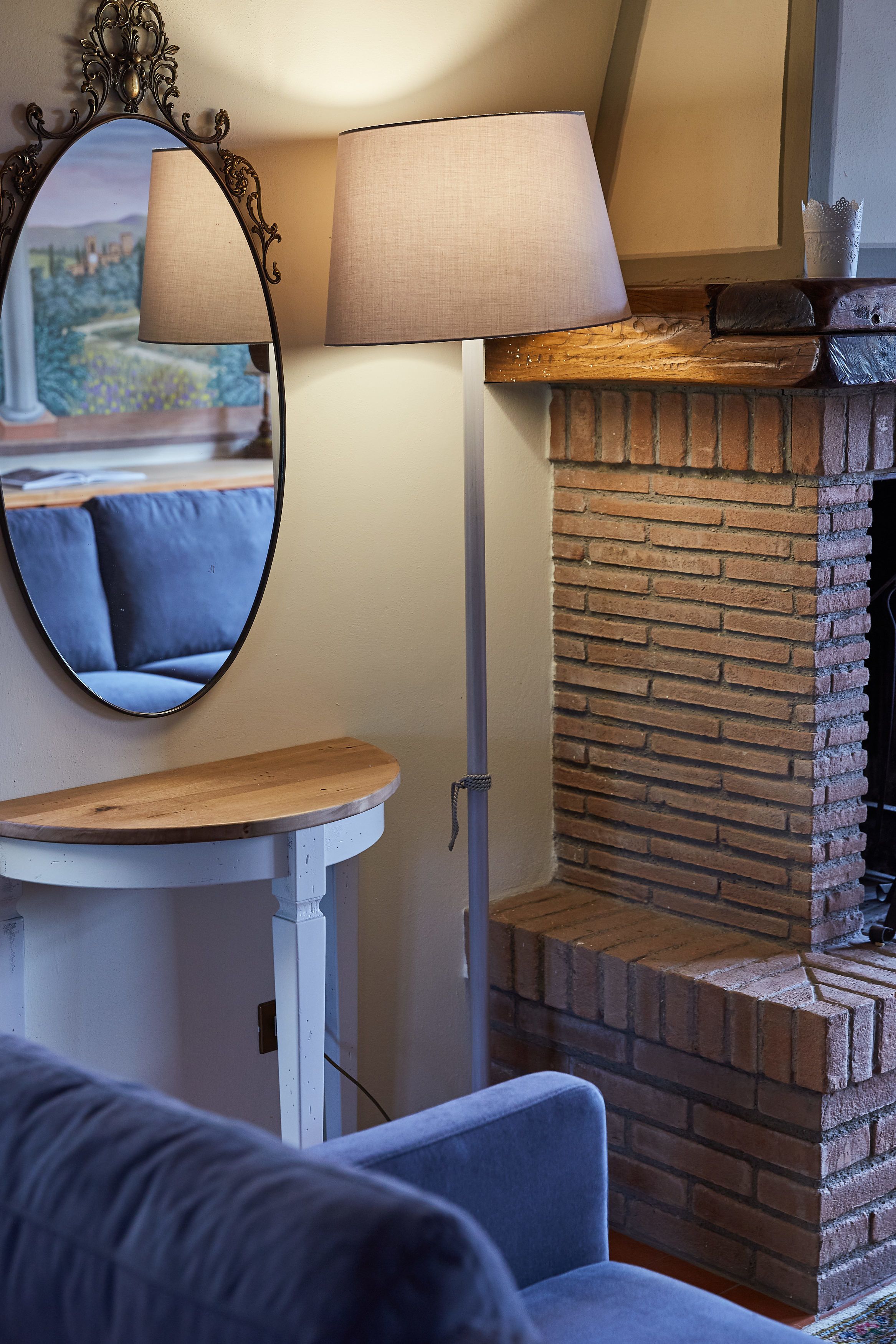 Ein gemütliches Wohnzimmer mit Kamin aus Ziegelsteinen, einem runden Spiegel, einer Lampe und einer hölzernen Bank.