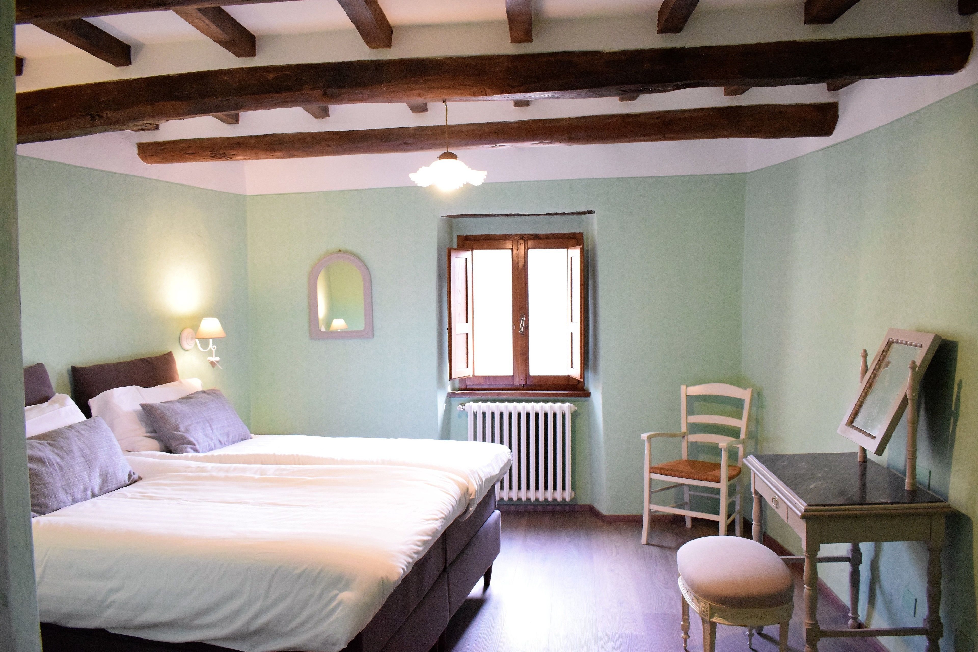 Une chambre à coucher avec un lit, une chaise, une table, une fenêtre et un radiateur.