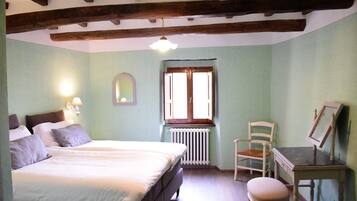 Une chambre à coucher avec un lit, une chaise, une table, une fenêtre et un radiateur.