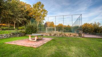 Ein Tennisplatz mit Netz, einer Steinmauer und einer Bank.
