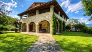 A stone building with a tiled roof, multiple arches, and a stone pathway leading to a covered patio area. - Fattorie di Celli (Poppi)