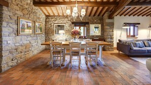 A rustic dining area with a stone wall, wooden beams, a brick floor, and a dining table with chairs. - Fattorie di Celli (Poppi)
