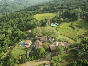 An aerial view of a rural property with multiple buildings, a swimming pool, and a large green field. - Fattorie di Celli (Poppi)