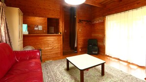A wooden cabin interior with a red sofa, a small table, a fan, and a window with curtains. - Kizin (Takamori)