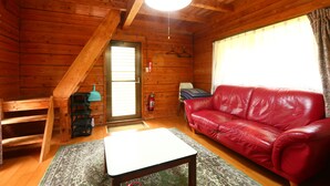 A wooden cabin interior with a red leather sofa, a small table, and a hanging light fixture. - Kizin (Takamori)