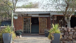 A reception area with a brick facade, a metal roof, and a wooden door. There are two large planters with plants in front. - OUT OF Nature Country Lodge (Windhoek)