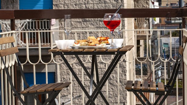 A balcony with a table set for a meal, a glass of red drink, and a view of the cityscape. - B&B Relax in Pompei (Pompei)