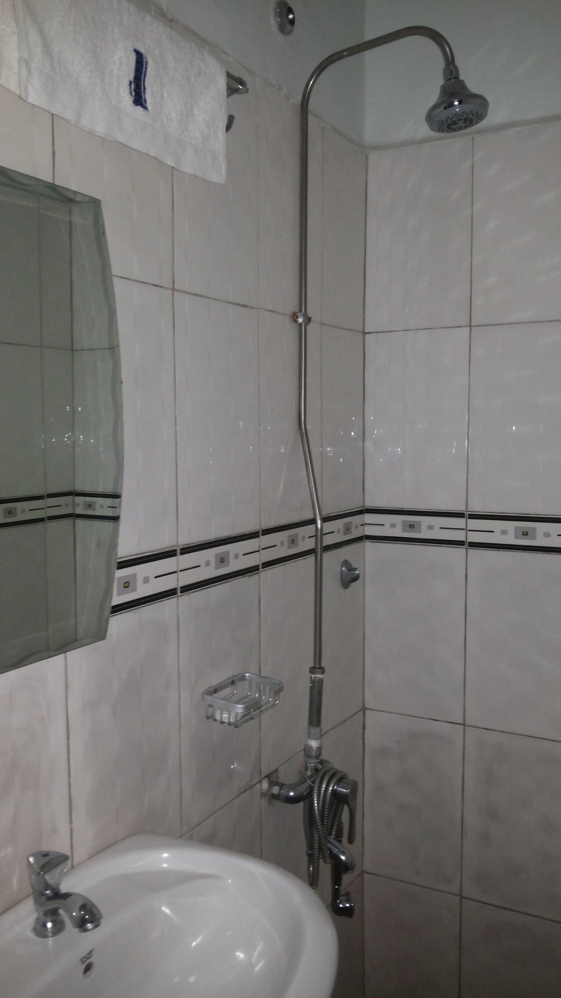 A bathroom with a white sink, a mirror, a shower with a handheld showerhead, and a soap dish.