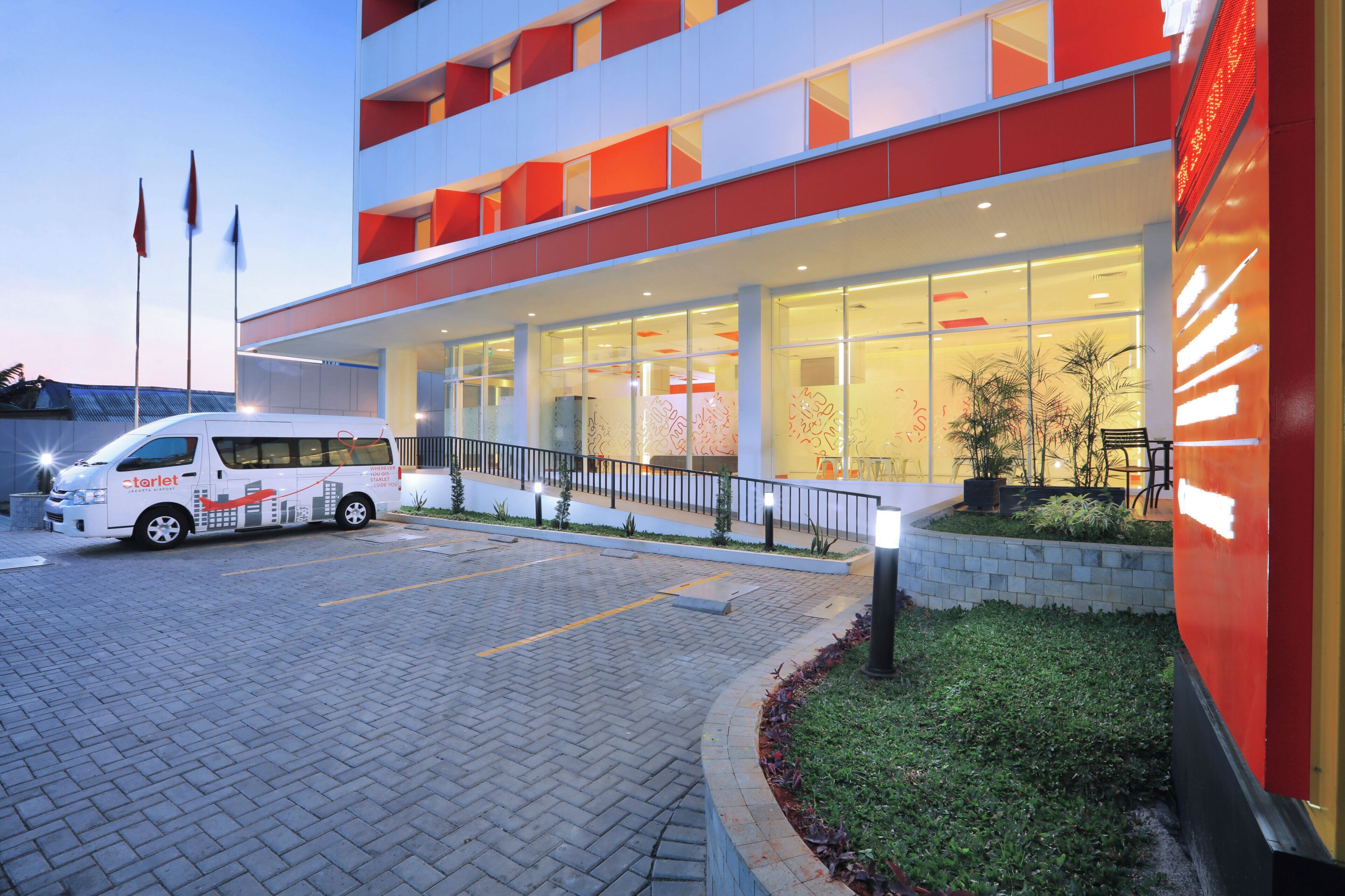 A modern building with a white and red facade, a parking area, and a bus parked in front.