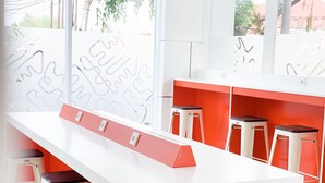 Una cocina moderna con encimeras blancas, detalles en rojo y taburetes de bar.