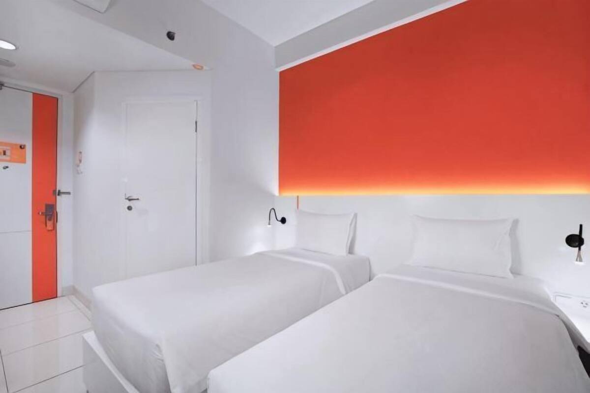 A hotel room with two beds, a white door, and a red accent wall.