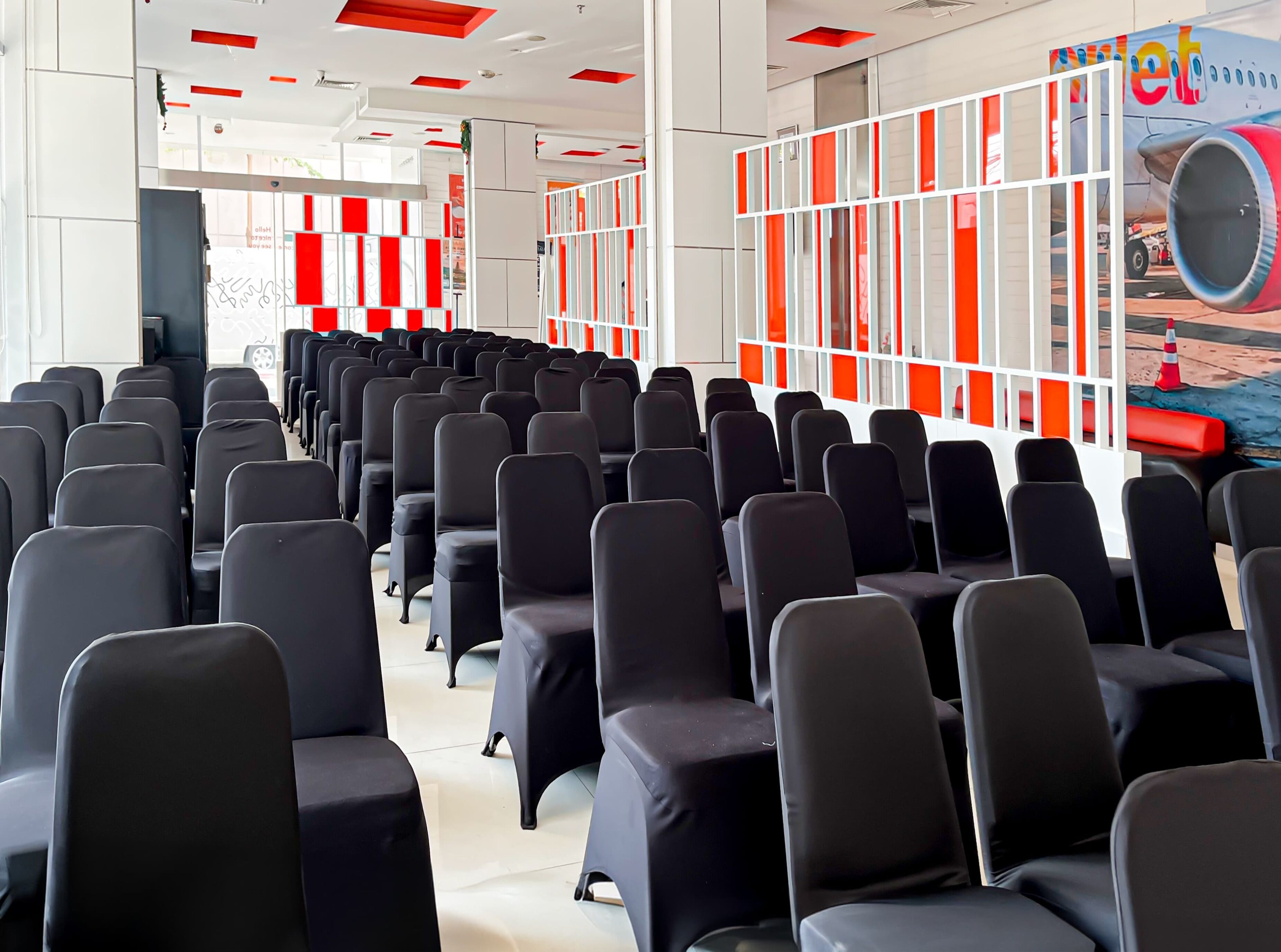 A conference room with rows of black chairs, white walls, and red accents.