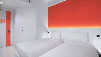 A hotel room with two beds, a white door, and a red accent wall.