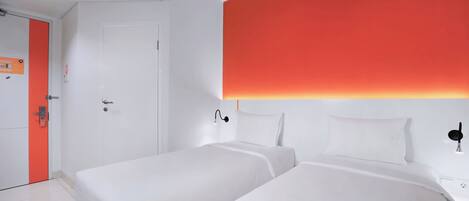 A hotel room with two beds, a white door, and a red accent wall.