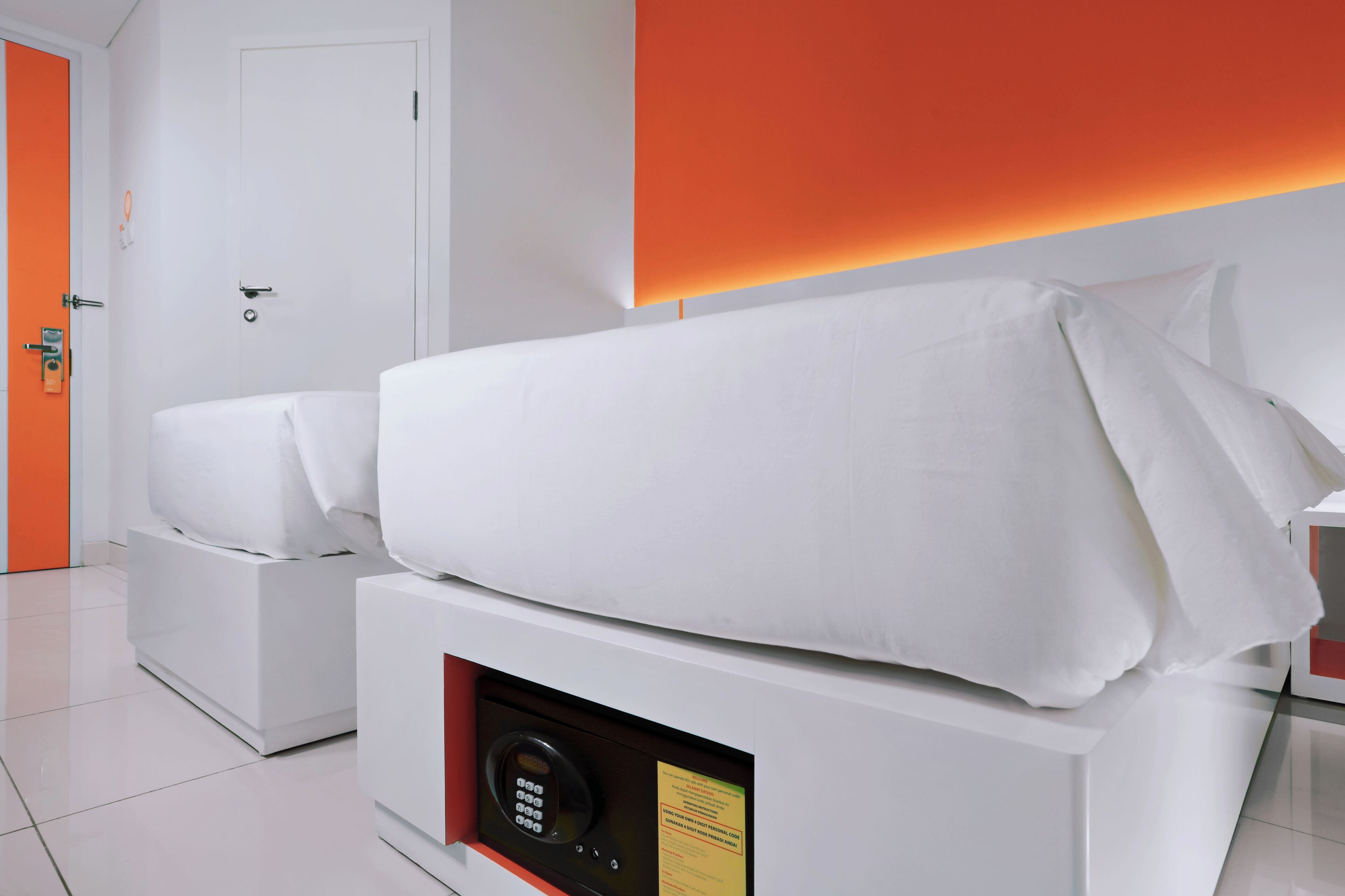 A modern hotel room with a bed, a control panel, and a door.