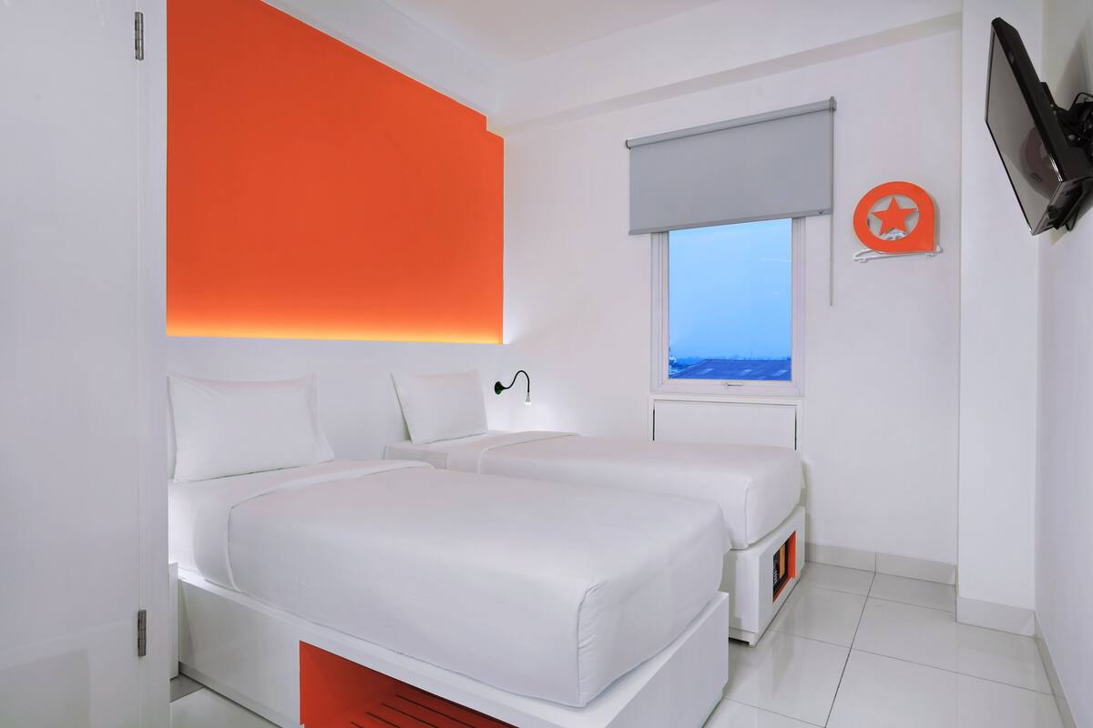 A modern hotel room with two beds, a large window with a view, and a mounted TV.