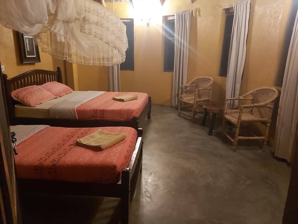 A room with two beds, a small table, and wicker chairs.