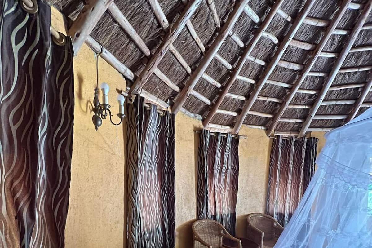 A room with a thatched roof, wicker furniture, and a mosquito net over the bed.