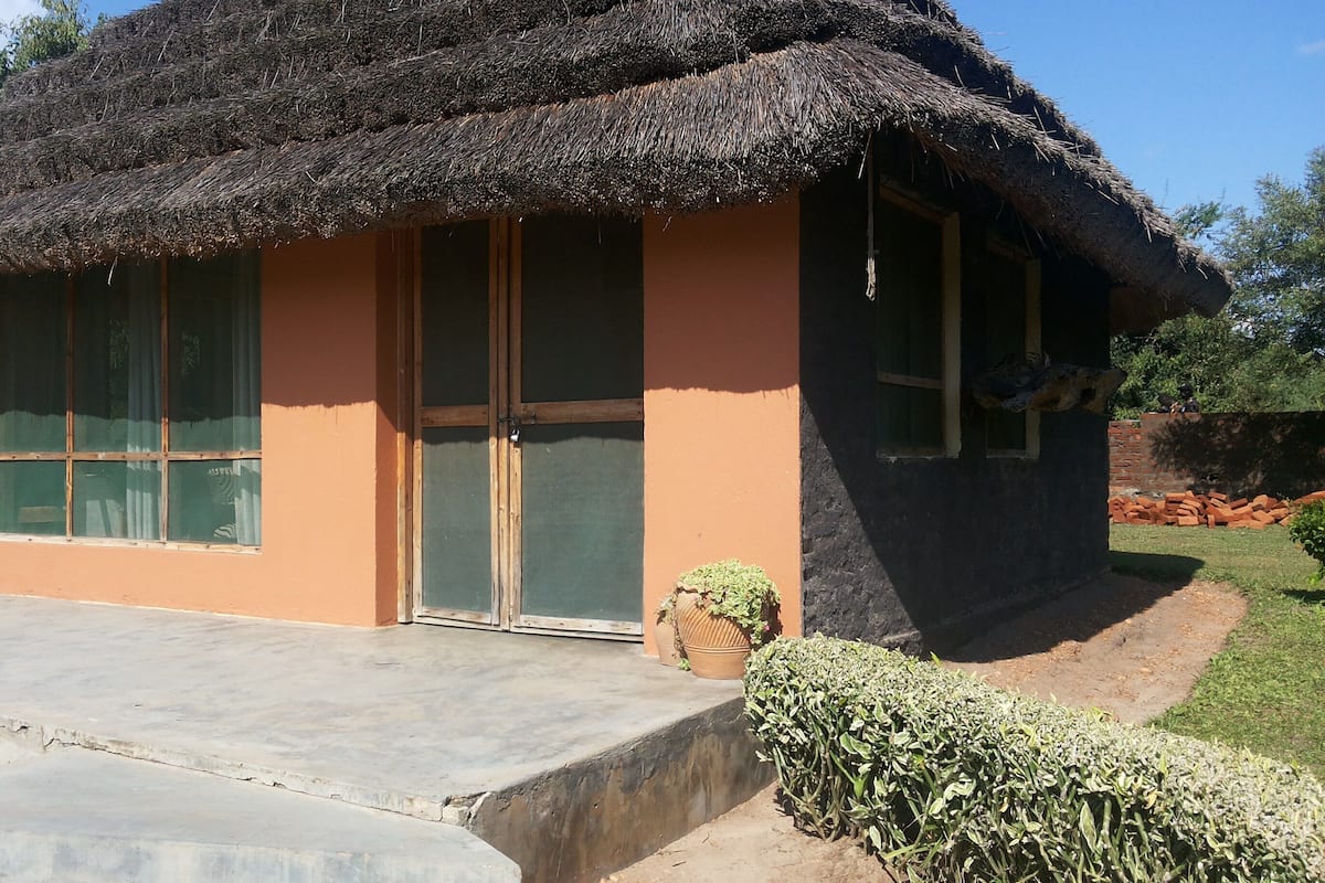 A single-story house with a thatched roof, large windows, and a concrete porch.