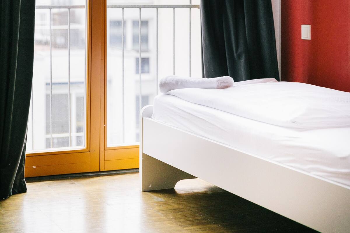 A hotel room with a bed, a sliding glass door to the outside, and a red wall.