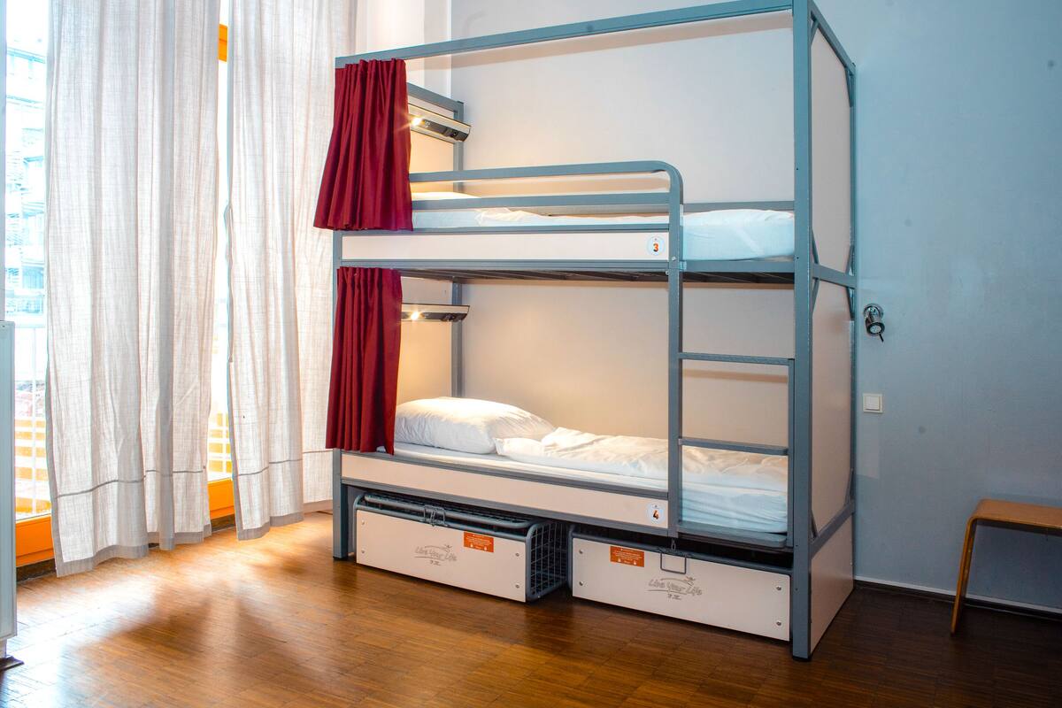A bunk bed with storage drawers, a window with curtains, and a wooden floor.