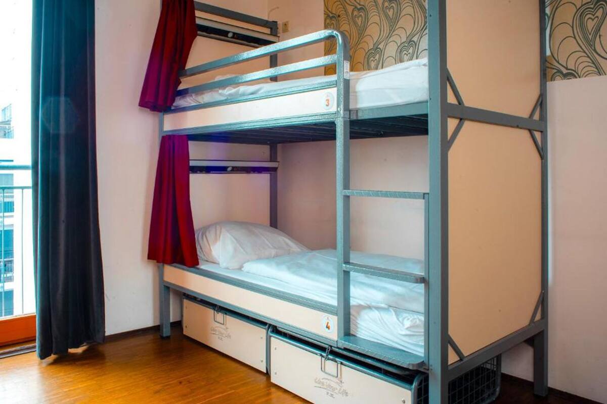 A bunk bed with a red curtain, wooden floor, and patterned wallpaper.