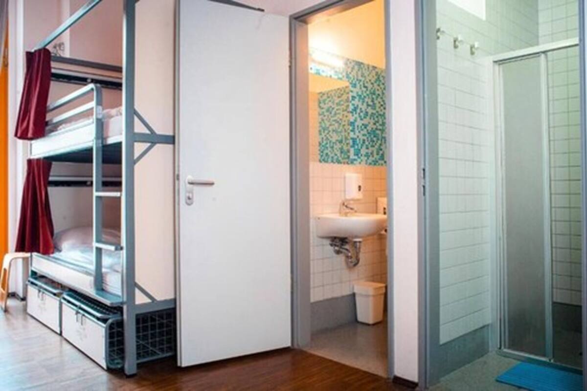 A room with bunk beds, a bathroom with a sink and tiled walls, and a shower area.