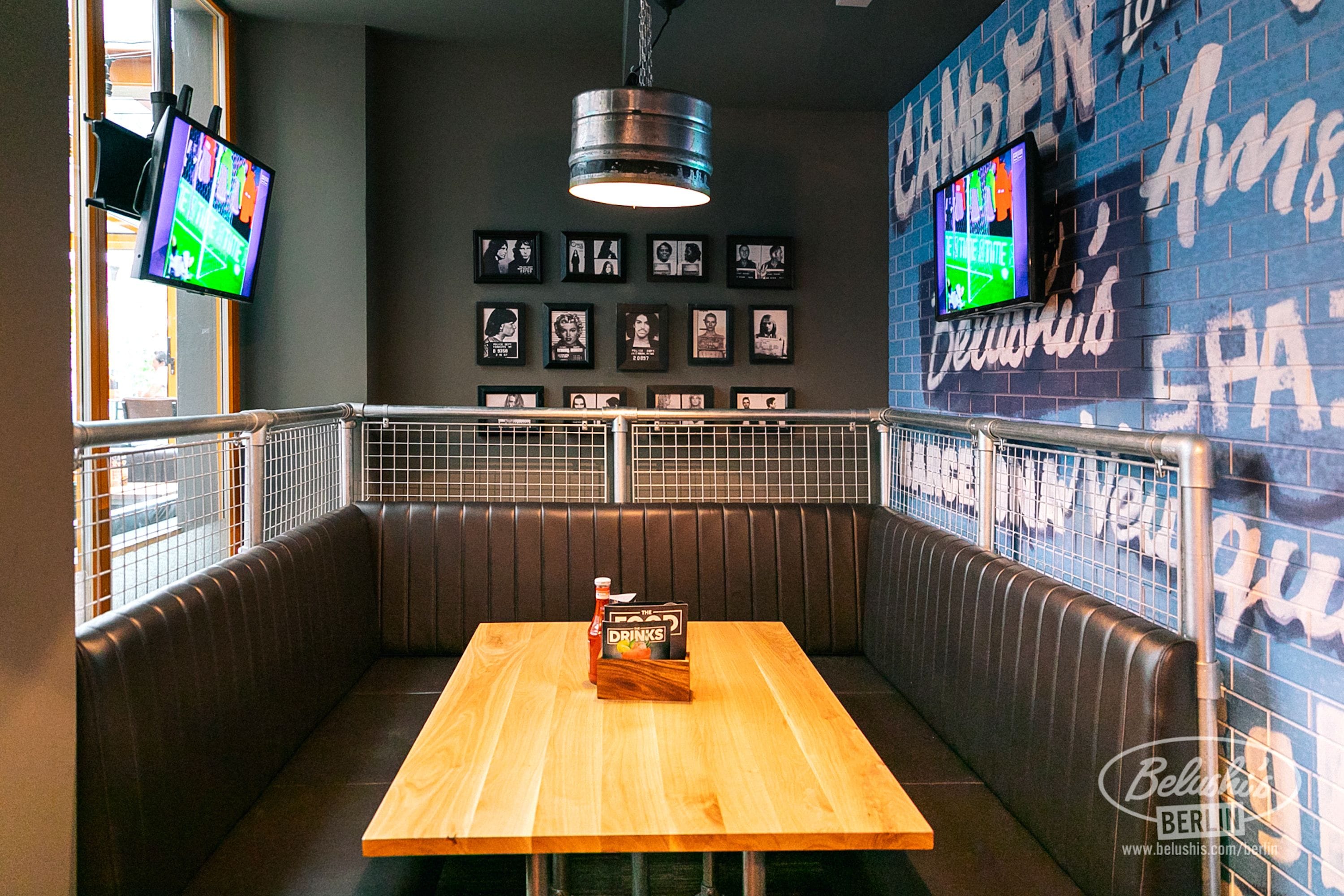 A restaurant interior with a wooden table, cushioned booths, framed pictures on the wall, and two TVs mounted on the wall.