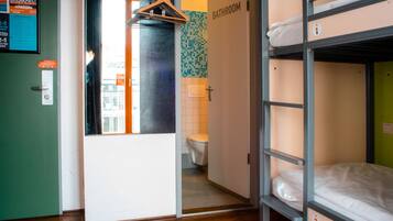 Habitación con literas, una puerta de baño, perchero y un inodoro a la vista.