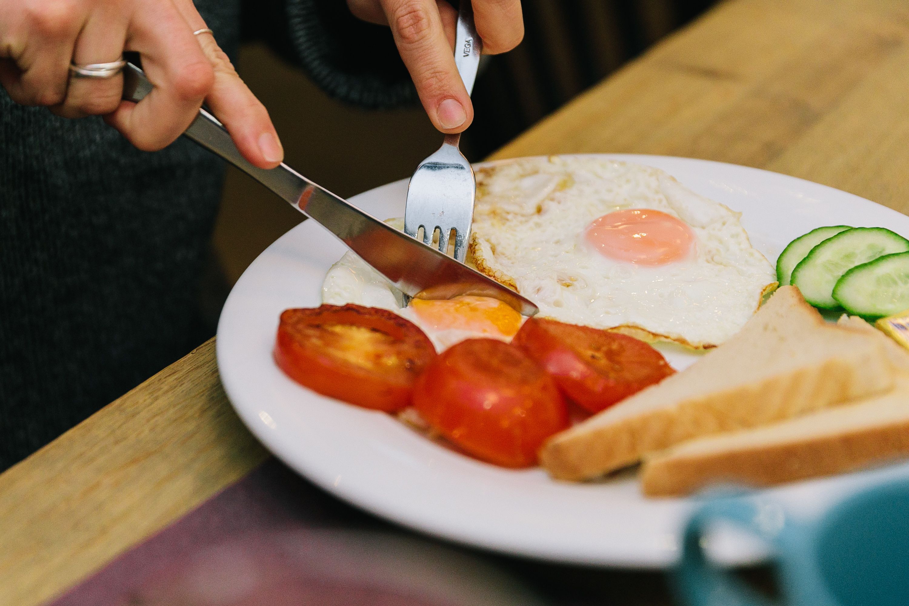 A plate with a fried egg, tomatoes, cucumber slices, and a slice of bread.