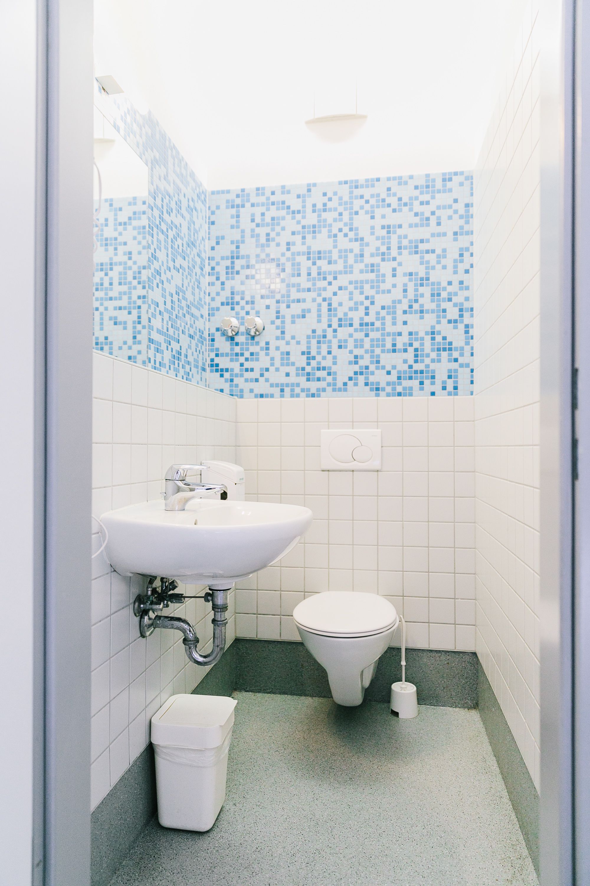 A small bathroom with a white sink, toilet, and trash bin.