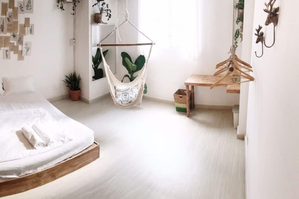 A modern bedroom with a bed, a hanging chair, a wooden bench, and a wall-mounted plant hanger.