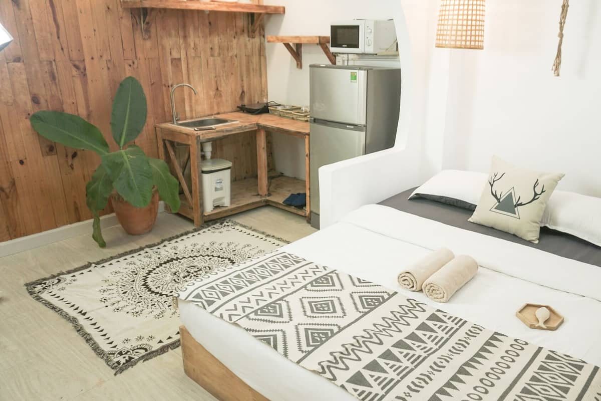 A compact bedroom with a bed, bedside table, and a small desk area with a microwave and refrigerator.