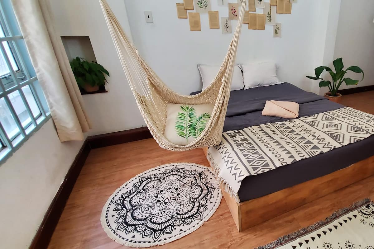 A bedroom with a bed, a hammock, a patterned rug, and a refrigerator.